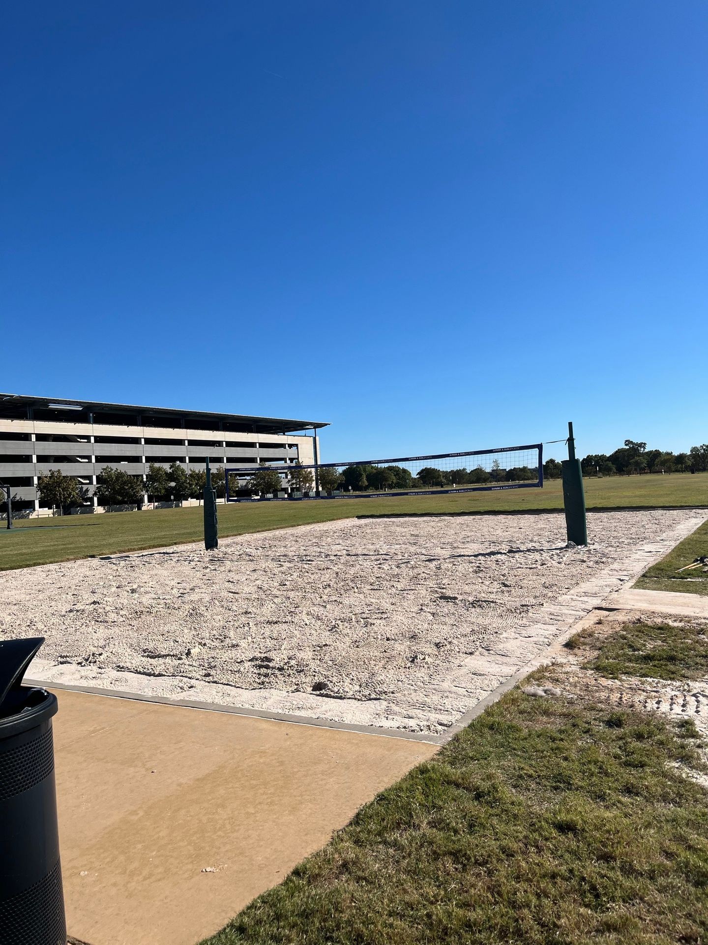 Outdoor sand volleyball court with net, padded posts, and surrounding grass