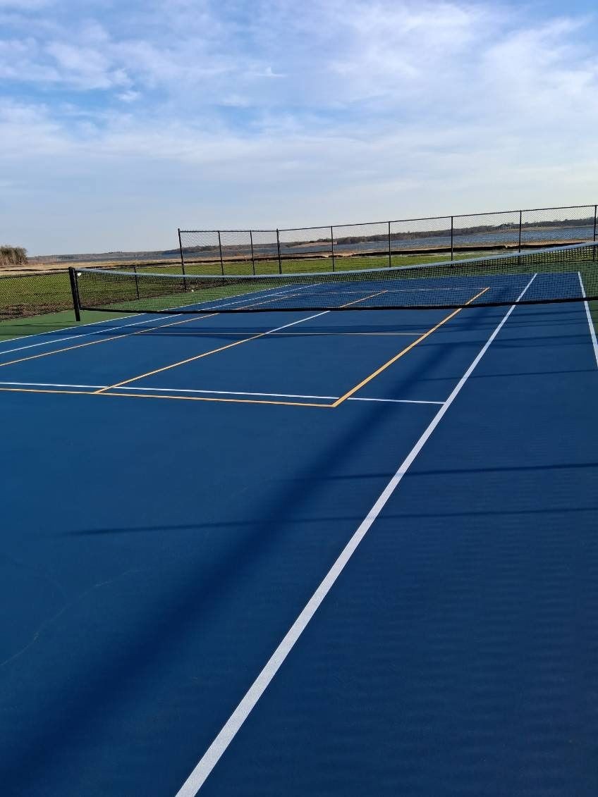 Blue outdoor tennis court with white tennis lines, yellow pickleball markings, and perimeter fencing Blue outdoor tennis court with white tennis lines, yellow pickleball markings, and perimeter fencing