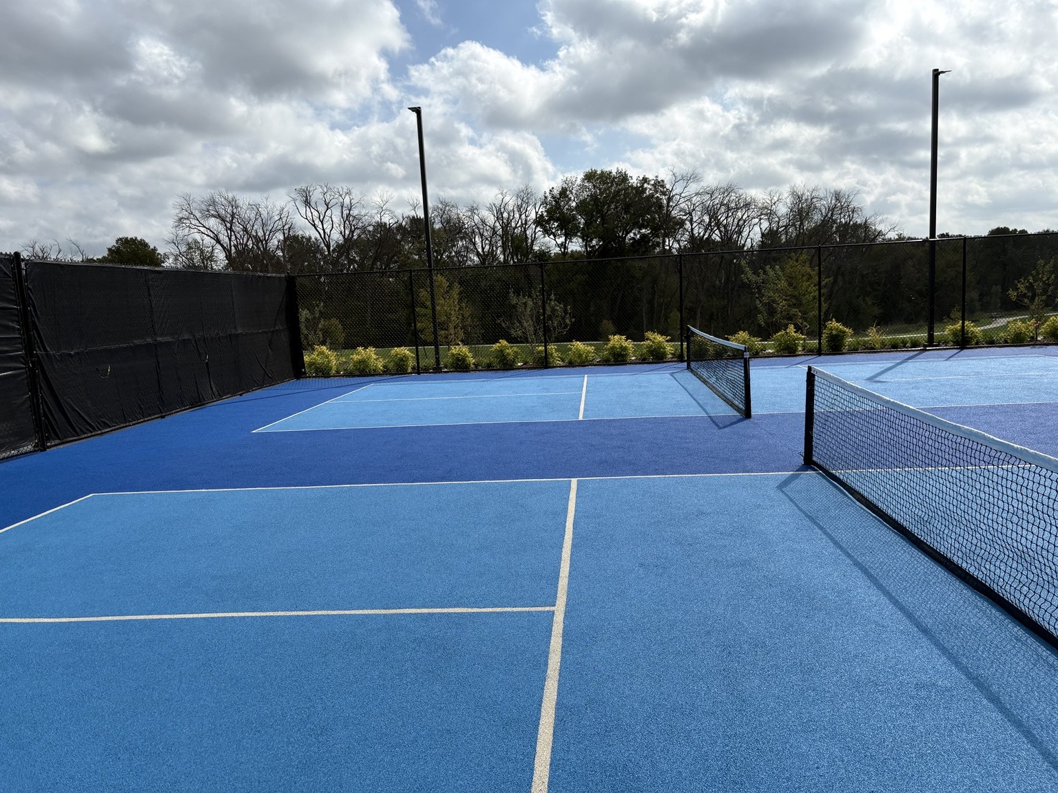 Blue rubber pickleball courts with nets and perimeter fencing